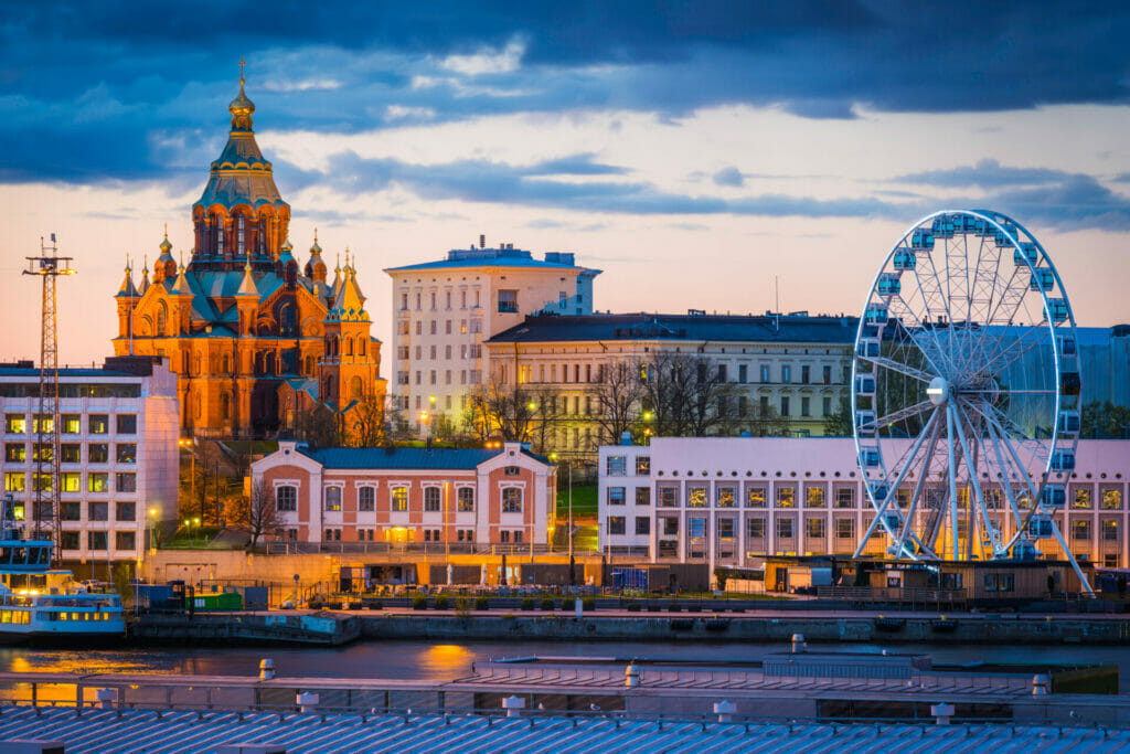 The iconic domes of Uspenski Cathedral spotlit against the sunset sky overlooking the ferris wheel and redeveloped warehouses on the waterfront of Helsinki harbour in the heart of Finland's vibrant capital city.