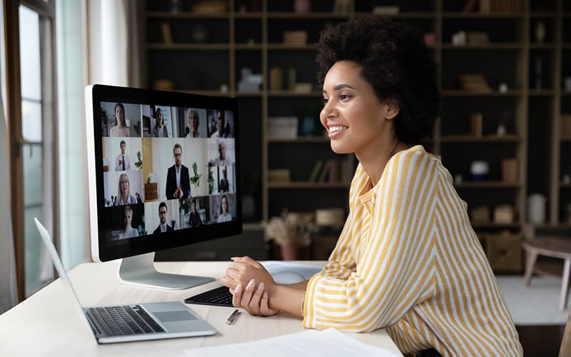 Happy African American remote employee talking on video conference call to colleagues, sitting at computer monitor, speaking to audience, attending virtual business meeting, negotiations, seminar